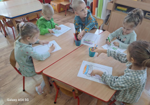 Dzieci wykonują pracę plastyczną przy stolikach.