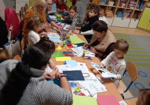 Rodzice z dziećmi siedzą przy stolikach i wykonują ozdoby świąteczne
