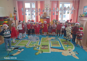 Dzieci ubrane w kolorze czerwonym i w mikołajowe czapki pozują do zdjęcia grupowego.
