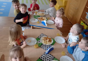 Dzieci siedzą przy stoliku i jedzą przygotowany poczęstunek