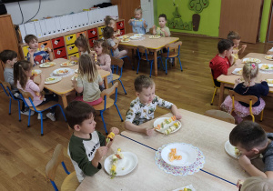 Dzieci siedzą przy stolikach i jedzą szaszłyki