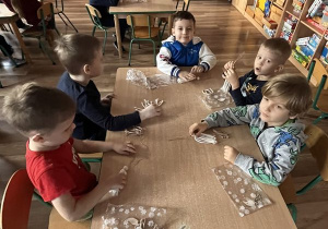 Dzieci siedzą przy stoliku i tworzą swoje aniołki
