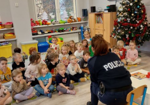Dzieci siedzą na dywanie i patrzą na policjantę