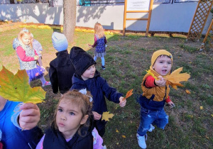 Dzieci zbierają liście pod klonem.