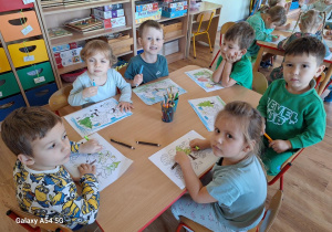 Dzieci kolorują przy stoliku obrazek konturowy "Drzewa".