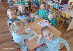 Dzieci kolorują przy stoliku obrazek konturowy "Drzewa".
