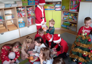 Oliwier przebrany w strój Mikołaja rozdaje dzieciom paczki