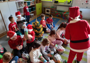 Oliwier przebrany w strój Mikołaja rozdaje dzieciom paczki