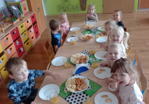 Dzieci siedzą przy stoliku i jedzą przygotowany poczęstunek