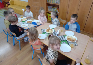 Dzieci siedzą przy stoliku i jedzą przygotowany poczęstunek