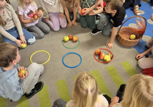 Dzieci uczestniczą w zabawie matematycznej - układają jabłka w kółkach wg, ilości podanej przez nauczyciela
