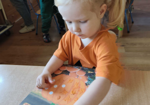 Gabrysia wykleja papierową dynię plasteliną