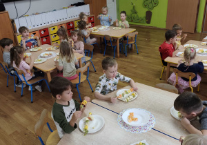 Dzieci siedzą przy stolikach i jedzą szaszłyki