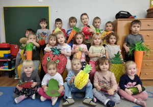 Dzieci pozują do zdjęcia z sylwetami owoców i warzyw.