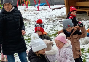 Rozbawione dzieci biegają po snieżnym ogrodzie przy pani