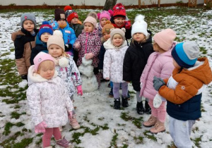 Dzieci pozują do zdjęcia, w środku stoi ulepiony bałwanek