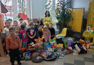 Dzieci pozują do zdjęcia na tle zgromadzonych darów