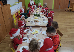 Dzieci siedzą przy stolikach podczas mikołajkowego poczęstunku