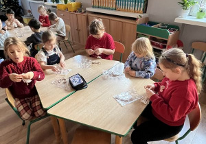 Dzieci siedzą przy stoliku i tworzą swoje aniołki