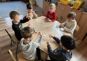 Dzieci siedzą przy stoliku i tworzą swoje aniołki