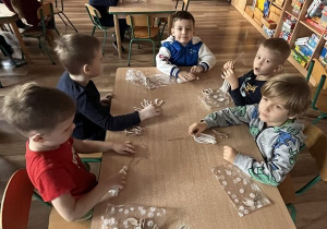 Dzieci siedzą przy stoliku i tworzą swoje aniołki