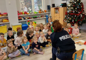 Dzieci siedzą na dywanie i patrzą na policjantę
