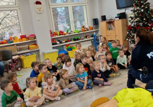 Dzieci siedzą na dywanie i patrzą na policjantę