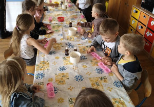 Dzieci siedzą przy stole i oglądają zgromadzone na nim akcesoria