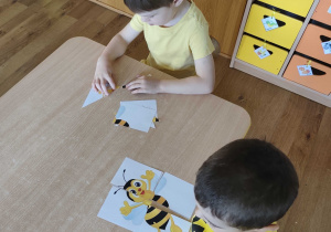 Dzieci układają puzzle z wizerunkiem pszczoły