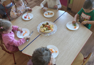 Dzieci siedzą przy stolikach i kroją owoce na sałatkę owocową