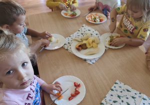 Dzieci siedzą przy stolikach i kroją owoce na sałatkę owocową