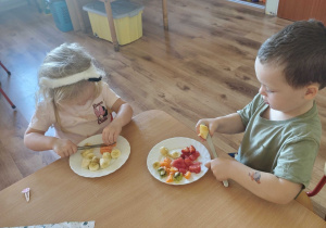 Dzieci siedzą przy stolikach i kroją owoce na sałatkę owocową