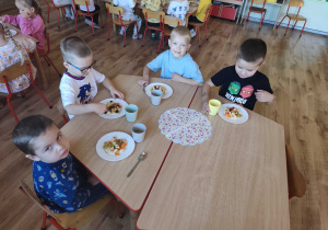 Dzieci siedzą przy stolikach i kroją owoce na sałatkę owocową