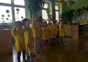Dzieci ubrane w żółte koszulki z logo naszego przedszkola pasowane na przedszkolaków ilustrują tekst piosenki "Zabawa przy słoneczku" ruchem