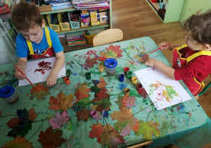 Chłopcy robią odciski z pomalowanych farbą liści.