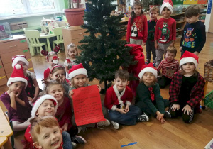 Dzieci siedzą pod choinką i pokazuja list od Świętego Mikołaja.