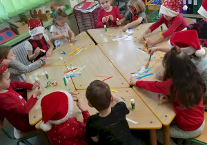 Dzieci z pasków kolorowego papieru robią łańcuch na choinkę.