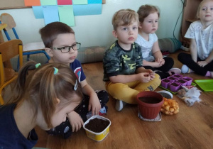 Dzieci siedzą na podłodze, czekają na posadzenie cebulek