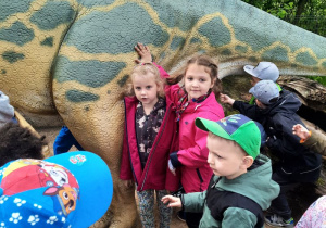 Dzieci pozują do zdjęcia, dotykając postaci dinozaura