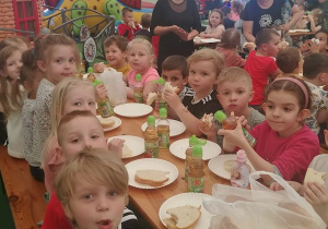 Po wielu atrakcjach czas na wspólny posiłek. Dzieci siedzą przy stole i jedzą kanapki.