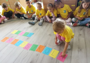 Dzieci na podłodze układają napis "Dzień Przedszkolaka" z kolorowych kartoników z literami.