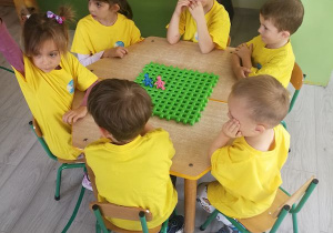 Dzieci siedząc przy stolikach udzielają odpowiedzi na temat naszego przedszkola i otrzymane punkty zamieszczają na kratownicy.
