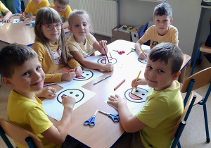 Dzieci siedzące przy stoliku kolorują emotkę uśmiechu.