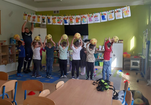 Dzieci ustawione w dwóch szeregach naprzeciwko siebie stoją z piłkami uniesionymi nad głowami.