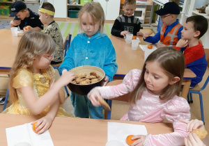 Ania przebrana za Ciasteczkowego Potwora częstuje dzieci ciasteczkami.