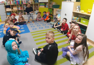 Dzieci przebrane w bajkowe stroje, siedząc w kole słuchają bajki czytanej przez nauczycielkę.