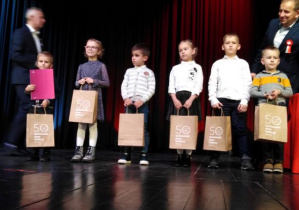 Dzieci stoją na scenie i pozują do zdjęcia widać osoby, ktore wręczały nagrody