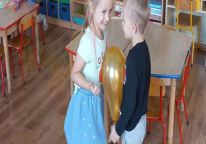 Lucynka i Adaś próbują wspólnie przenieść balon bez użycia rąk.