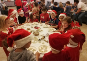 Dzieci stojąc przy jednym stole wycinają foremkami kształty pierniczków.