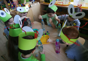 Dzieci wsypują do napełnionych wodą butelek drobne elementy i kolorową bibułę tworząc "Kosmos w butelce".